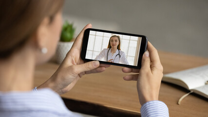 Close up view of woman talk speak on video call on smartphone with young Caucasian nurse or doctor. Female have online webcam consultation with GP or therapist on cellphone. Virtual event concept.