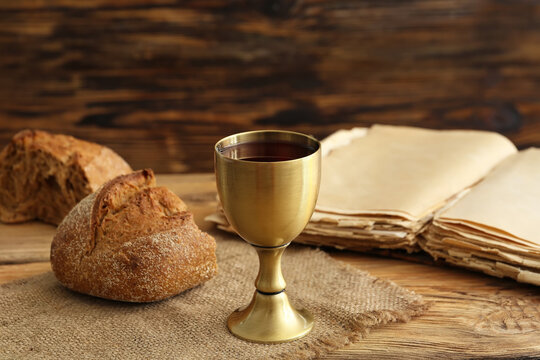 Chalice of wine with bread and Holy Bible on wooden background