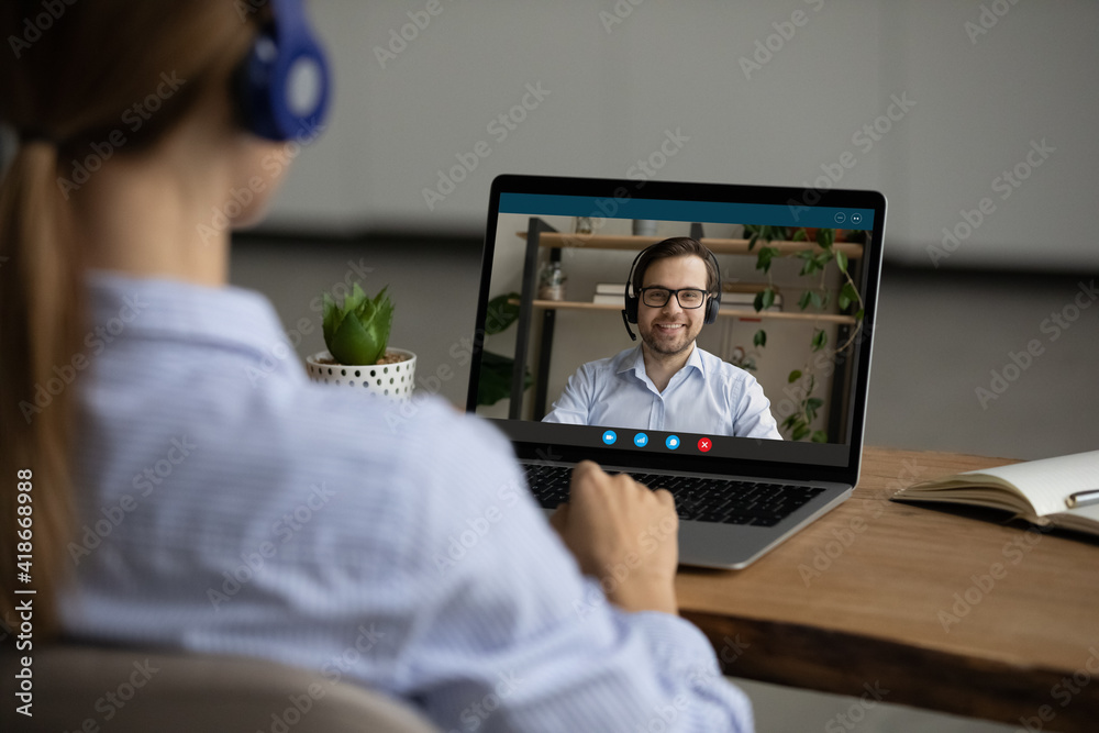 Poster back view of woman in headphones look at laptop screen talk speak on video call with male colleague.