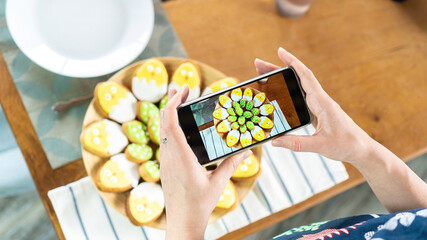 A food blogger takes pictures of an egg-shaped Easter sugar cookie on a smartphone. The influencer...