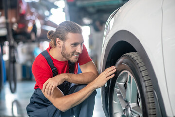 Man in overalls crouched near car wheel