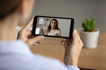 Close up back view of female watch online lesson or coach webinar on cellphone gadget. Woman talk...