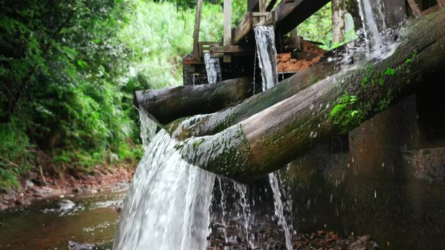 Water coming out of bamboo pipes that are connected to water hammers to smash clay in the process of making an Ontayaki, a Japanese handmade spiral pattern plate and pottery, in nature surrounded. 