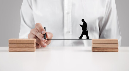Male hand draws a line between the wooden blocks for a businessman silhouette to walk across.