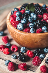 Ripe blackberries with leaves in a bowl on a wooden board on a dark background