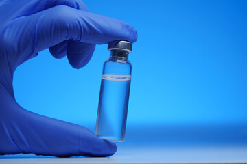 Glass bottle with liquid in the hand of a doctor in blue medical gloves close-up. Insulin or vaccine in a flask. Doctor demonstrates a bottle with a medicine