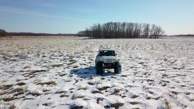 View from above. Inspector raid on a winter reserve in Russia on a swamp vehicle. A jeep on large wheels drives through a snow-covered field.