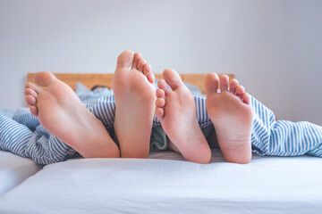 Couple is enjoying the morning in bed: Close up of uncovered feet in the bed, blanket