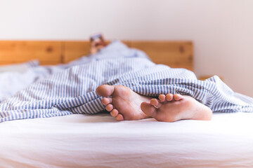 Couple is enjoying the morning in bed: Close up of uncovered feet in the bed, blanket