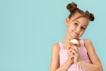 adorable little girl eating vanilla ice cream in waffle cone on blue background. copy space