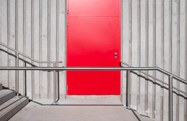 Aufnahme einer roten Türe nächst einer Treppe mit Handlauf aus Edelstahl