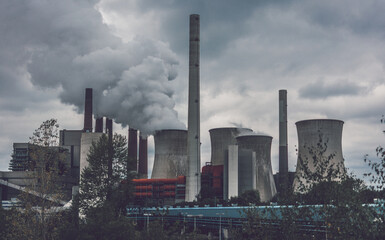 View of coal power plant against sun with several chimneys and huge fumes