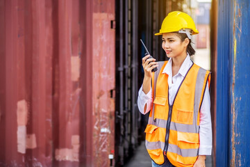 Young confident woman engineer smiling and using radio communication and wearing yellow safety helmet and check for control loading containers box from Cargo freight ship for import and export