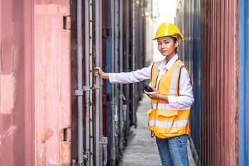 Young confident woman engineer using radio communication and wearing yellow safety helmet and check for control loading containers box from Cargo freight ship for import and export