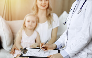 Obraz premium Doctor and patient. Pediatrician using clipboard while examining little girl with her mother at home. Sick and unhappy child at medical exam