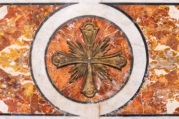 Close-up on golden metal cross on decorated marble wall inside catholic roman church