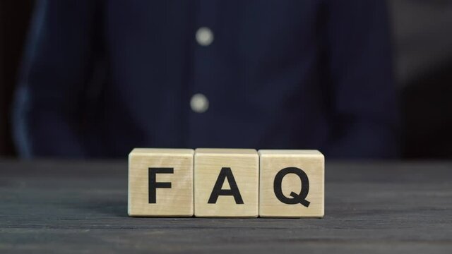 A man in a shirt showing the word FAQ from wooden cubes, close up
