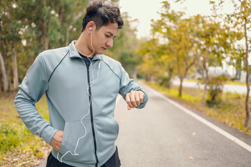 Happy sport man in earphone listen music standing and looking at smartwatch during training and running in the park.