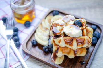 Fresh sliced banana fruit and blueberry on top of delicous homemade waffle in dark brown wooden plate ready for breakfast time