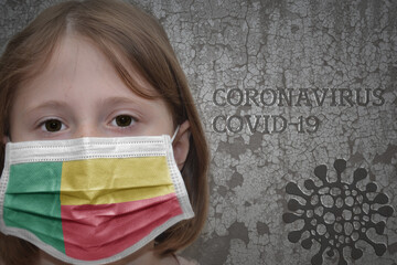 Little girl in medical mask with flag of benin stands near the old vintage wall with text coronavirus, covid, and virus picture.