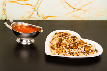 Famous traditional Arabic, Egyptian dish - Koshari. National Kushari in a white plate on dark wooden background with tomato sauce