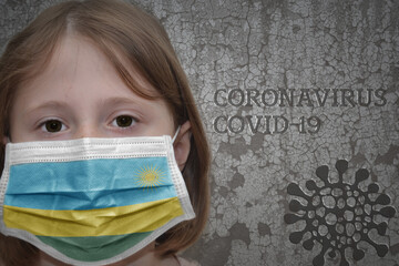 Little girl in medical mask with flag of rwanda stands near the old vintage wall with text coronavirus, covid, and virus picture.