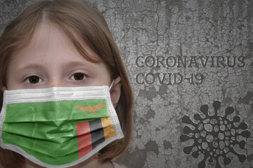 Little girl in medical mask with flag of zambia stands near the old vintage wall with text coronavirus, covid, and virus picture.