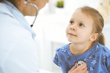 Doctor examining a little girl by stethoscope. Happy smiling child patient at usual medical inspection. Medicine and healthcare concepts