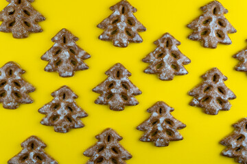 Christmas tree cookies on yellow background. New Year's food. Festive baked goods. Gingerbread on the table. Icing sugar sweetness taste season. Pattern