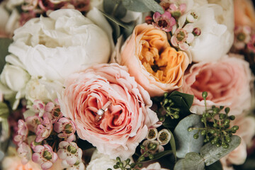 Wedding details. The bride's ring with a diamond lies on a flower of a bouquet of peonies and eucalyptus