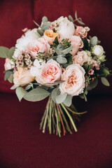 Wedding details. The bride's bouquet of white and pink flowers with greenery and eucalyptus stands on an armchair with burgundy upholstery