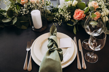 Wedding banquet. The festive table is served with plates with napkins and name cards, glasses and cutlery, and decorated with flower arrangements and candles
