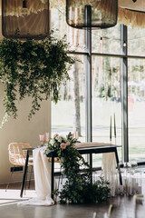 Wedding banquet. In the bright room there is a festive table decorated with compositions of flowers and candles, with a tablecloth, served with plates, glasses and cutlery