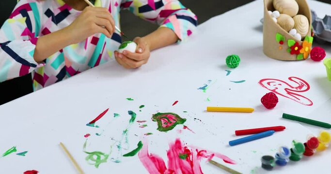Unrecognizable little girl painting, drawing with brush eggs at home