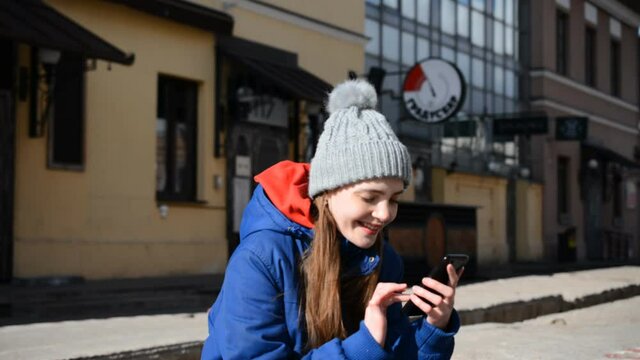 Cheerful young hipster girl chatting with friends on the phone on the street of her city on a spring sunny day