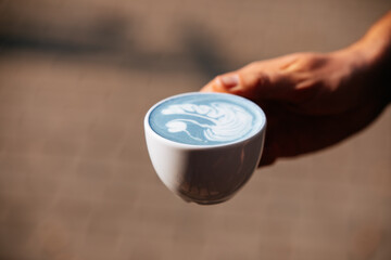 cup of blue coffee with a froth art drawing in hand