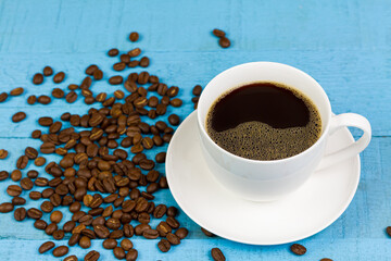 Black coffee in white ceramic cup with coffee bean on blue wooden background.