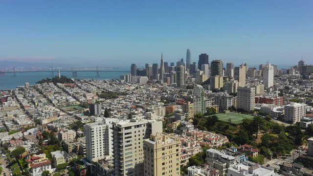 Aerial panning shot of city by famous bridge over sea against blue sky, drone flying over modern cityscape on sunny day - San Francisco, California