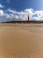 Vertical panorama image of the dutch island of Texel with red light house, blue sky and white clouds. Wave texture on the sand beach foreground