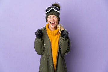 Skier Russian girl with snowboarding glasses isolated on purple background celebrating a victory in winner position