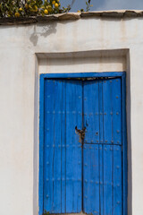 Old wooden door divided into three parts and painted blue on a white wall, closed by a chain with a padlock.