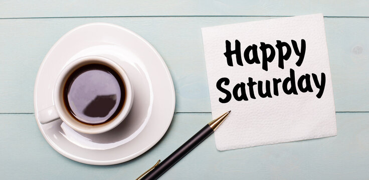 On a light blue wooden tray, there is a white cup of coffee, a handle and a napkin that says HAPPY SATURDAY