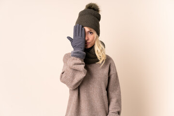 Young woman with winter hat over isolated background covering a eye by hand