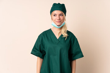 Surgeon woman in green uniform over isolated background standing and looking to the side