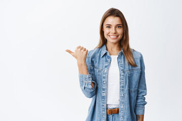 Confident young woman with assured smile pointing left at copy space logo, showing good deal, recommending product, white background - 418694741