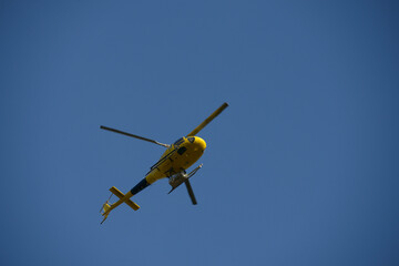 
Yellow helicopter in flight, hovering overhead