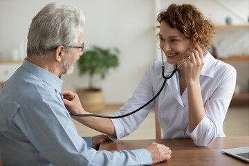 Smiling young Caucasian female doctor hold stethoscope listen to elderly male patient heart rate....
