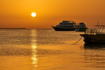 Naklejka premium Dawn at sea. The sun rises above the water against the background of the yacht