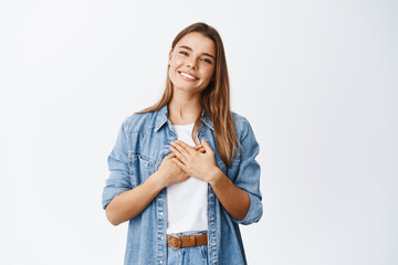 Portrait of touched young woman feeling flattered, holding hands on heart and smiling white teeth, say thank you, appreciate help, being grateful for nice gesture, white background - 418695549