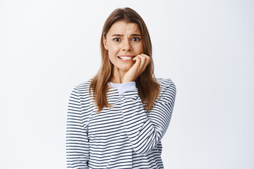 Scared blond girl biting nails on fingers and frowning, afraid of someone will know her little secret, standing anxious and panicking, white background